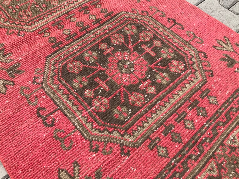 Puede incluir: Una alfombra roja y marr&oacute;n con un dise&ntilde;o geom&eacute;trico. La alfombra tiene un aspecto desgastado y est&aacute; hecha de un material tejido.
