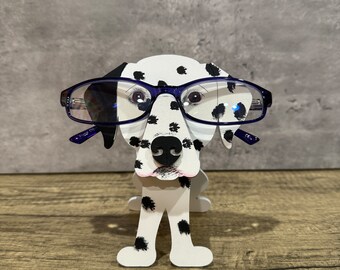 May include: A white and black Dalmatian dog figurine with blue glasses, used as a glasses holder.