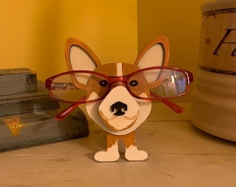 May include: A wooden dog figurine with red glasses, painted in brown, white, and black. The dog is standing on a wooden surface.