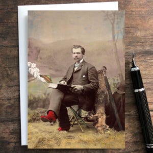 May include: A greeting card featuring a vintage-style portrait of a person in a brown suit and bright red boots sitting on a folding stool while reading a book. A small flying saucer with a trail of smoke is visible in the background sky.