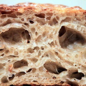 Puede incluir: Primer plano del interior de una hogaza de pan, mostrando la textura aireada y los grandes agujeros. El pan es de color marrón claro y tiene una corteza ligeramente crujiente.