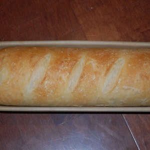 Könnte beinhalten: Ein frisch gebackenes Brot in einer Keramik-Brotform. Das Brot ist goldbraun und hat eine knusprige Kruste.