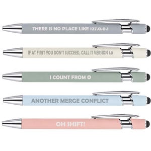 May include: Five retractable ballpoint pens with chrome accents and black stylus tips. Each pen features a unique matte barrel color and white text: THERE IS NO PLACE LIKE 127.0.0.1, IF AT FIRST YOU DON'T SUCCEED, CALL IT VERSION 1.0, I COUNT FROM 0, ANOTHER MERGE CONFLICT, and OH SHIFT!