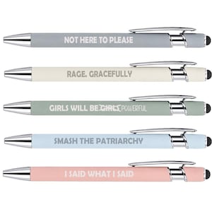 May include: A set of five retractable ballpoint pens with chrome accents and stylus tips. The pens are colored gray, cream, sage green, light blue, and pink. Each features white text: NOT HERE TO PLEASE, RAGE. GRACEFULLY, GIRLS WILL BE POWERFUL, SMASH THE PATRIARCHY, and I SAID WHAT I SAID.