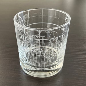 May include: A clear glass tumbler with an etched design of the city of Champaign, Illinois. The design includes street names and the text "Champaign" and "Campus Town".