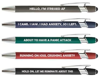 May include: A set of five retractable ballpoint pens with silver-toned clips and tips. Each pen features a unique color barrel and white text: HELLO, I'M STRESSED AF; I CAME. I SAW. I HAD ANXIETY, SO I LEFT.; ABOUT TO HAVE A PANIC ATTACK; RUNNING ON SOUL CRUSHING ANXIETY; HOLD ON, LET ME RUMINATE ABOUT THIS.