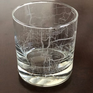 May include: A clear glass tumbler with an etched design of the Seattle city map. The map includes the Seattle University District, Belltown, and Greater Duwamish.