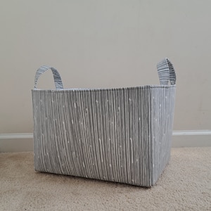 May include: A gray fabric storage bin with white stripes and two fabric handles. The bin is sitting on a light brown carpet.