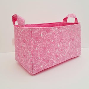 May include: Pink fabric storage bin with white swirl and star pattern and two handles.