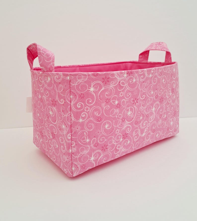 May include: Pink fabric storage bin with white swirl and star pattern and two handles.
