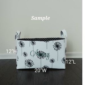 May include: White fabric storage bin with black and white dandelion print and black polka dot lining. The bin has two handles and measures 12 inches high, 20 inches wide, and 12 inches long. The bin is personalized with the name "Amy" in green embroidery.