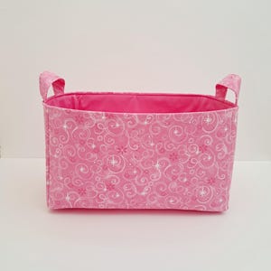 May include: Pink fabric storage basket with white swirl and star pattern and two handles.