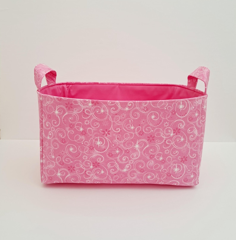 May include: Pink fabric storage basket with white swirl and star pattern and two handles.
