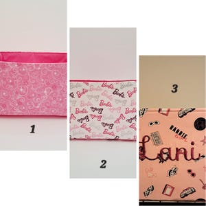 May include: Three pink fabric storage bins with different patterns. The first bin has a pink and white swirl pattern. The second bin has a white background with the word "Barbie" repeated in pink and black. The third bin has a pink background with a black and white pattern of sunglasses, a cassette tape, a car, and the words "Barbie Girl" and "Lani".