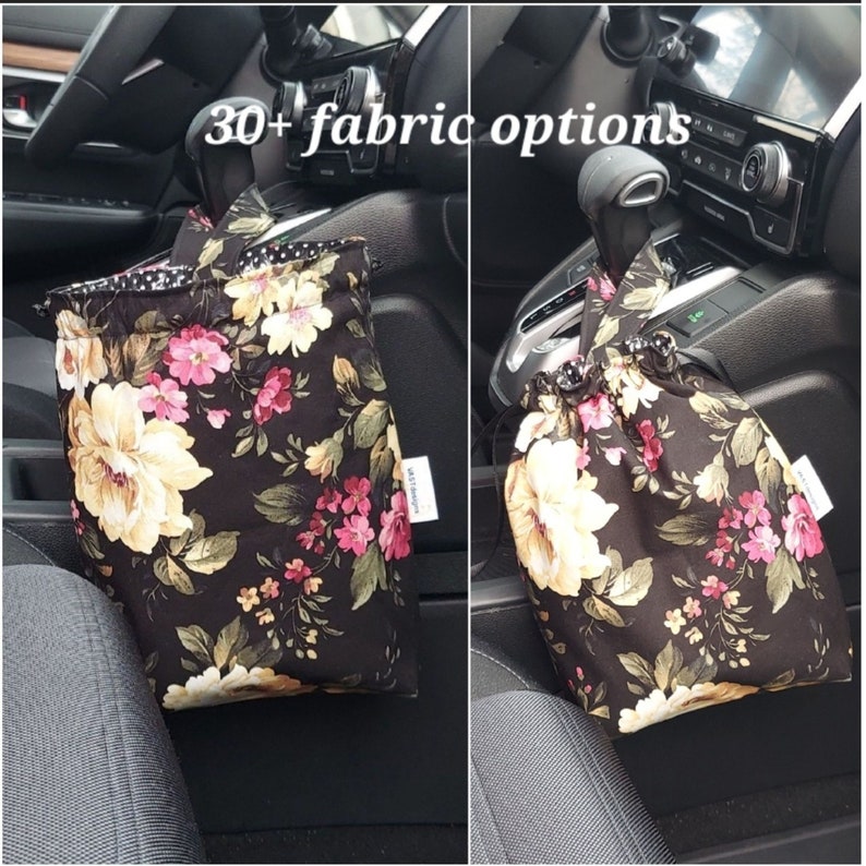 May include: Two black fabric bags with floral patterns hanging from the gear shift in a car. The bags have a drawstring closure and are labeled "30+ fabric options".
