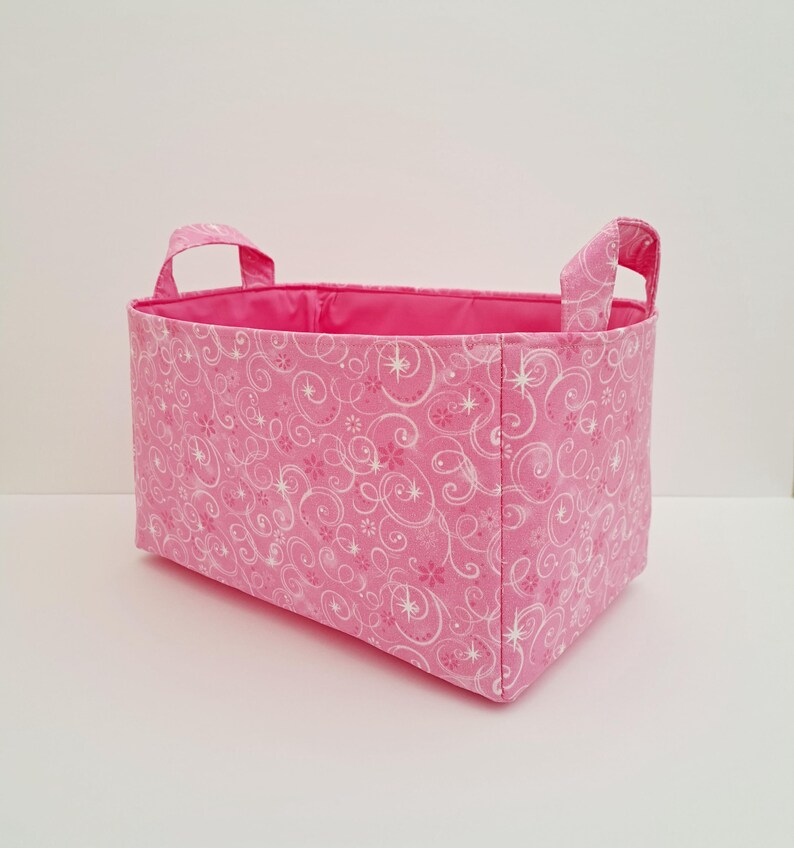 May include: Pink fabric storage basket with white swirl and star pattern and two fabric handles.