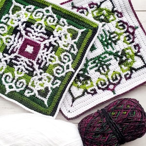 Puede incluir: Dos cuadrados tejidos a crochet con un patrón geométrico en tonos de verde, blanco y morado. Una bola de hilo en los mismos colores está en primer plano.