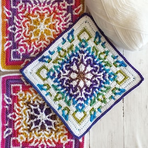 May include: Two colourful crochet squares with intricate geometric patterns in shades of purple, blue, green, yellow, orange, and pink. The squares are made with white yarn and have a white border.