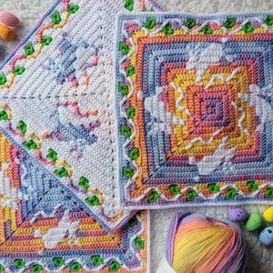 May include: Three colorful crocheted squares with a pastel color scheme. The squares feature intricate patterns and are decorated with green leaf accents. A ball of yarn and decorative Easter eggs are also present.