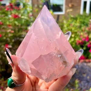 May include: A large, pink rose quartz crystal in the shape of a pyramid. The crystal is clear and has a smooth, polished surface.