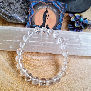 Könnte beinhalten: Ein Armband aus klaren Quarzkristallperlen mit einem schlichten Design. Das Armband besteht aus runden, glatten Perlen und ist auf einer durchsichtigen Gummikordel aufgefädelt.