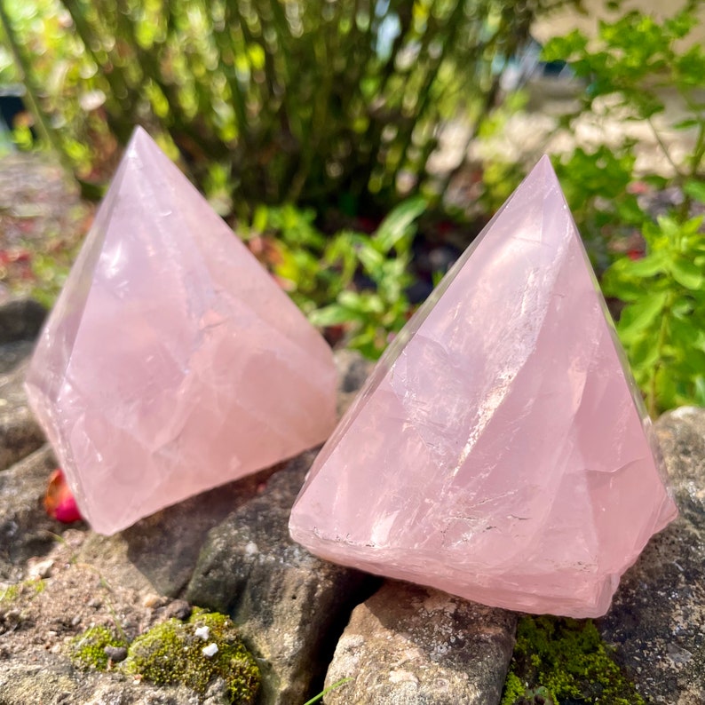 May include: Two pink rose quartz crystal pyramids. The pyramids are smooth and have a translucent appearance.