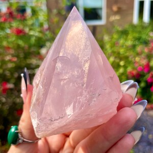 May include: A large, pale pink rose quartz crystal in the shape of a pyramid. The crystal is translucent and has a slight shimmer.