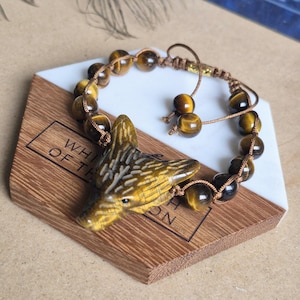 May include: A bracelet featuring round, polished tiger's eye beads and a carved tiger's eye wolf head pendant. The beads are strung on a brown cord with an adjustable sliding knot closure, finished with two smaller tiger's eye beads at the ends.