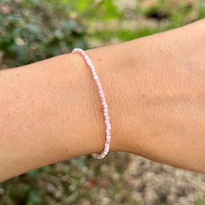 Peut inclure: Un bracelet délicat en perles roses avec de petites perles rondes. Le bracelet est porté au poignet.