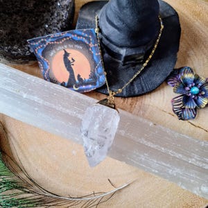 May include: A clear, raw quartz crystal pendant hangs from a gold-toned chain. The necklace is displayed with a rectangular card featuring a silhouette of a witch and cat against a moon, with the text White Witch of the Moon printed on it.