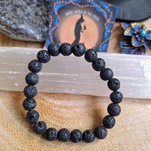 May include: A black lava rock beaded bracelet. The bracelet is made of round, black beads with a rough, textured surface.