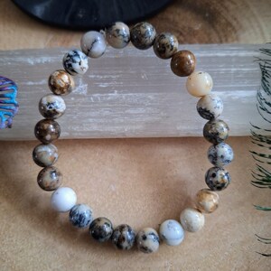 May include: A brown, white, and black patterned stone bead bracelet. The beads are round and have a natural, polished finish.