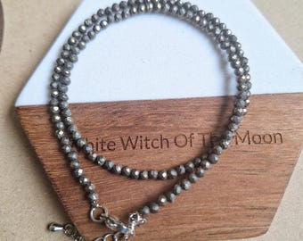May include: A necklace made of small, grey, faceted beads. The necklace is displayed on a wooden and white hexagonal coaster with the text "White Witch Of The Moon". The necklace has a silver clasp.
