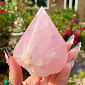 May include: A large, light pink rose quartz crystal in the shape of a pyramid. The crystal is smooth and polished, with a slight translucence.