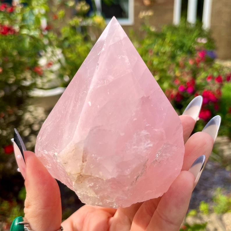 May include: A large, light pink rose quartz crystal in the shape of a pyramid. The crystal is smooth and polished, with a slight translucence.