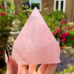 May include: A large, pale pink rose quartz crystal pyramid. The pyramid is smooth and polished, with a slightly translucent appearance.