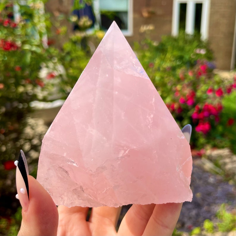 May include: A large, pale pink rose quartz crystal pyramid. The pyramid is smooth and polished, with a slightly translucent appearance.