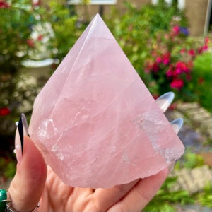 May include: A large, pink rose quartz crystal pyramid. The crystal is smooth and polished, with a natural, slightly rough base.