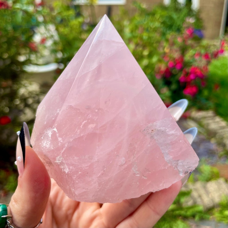 May include: A large, pink rose quartz crystal pyramid. The crystal is smooth and polished, with a natural, slightly rough base.