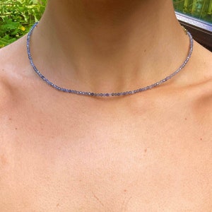 May include: A delicate necklace made of small, light blue beads. The necklace is worn by a person, but the focus is on the necklace itself.