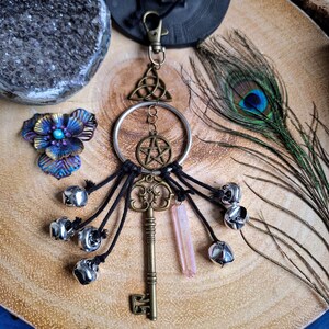 Puede incluir: Un amuleto de llave de plata con un pentagrama, un nudo celta y un colgante de cristal. El amuleto est&aacute; unido a un anillo de plata y tiene varias campanillas de plata colgando de &eacute;l.