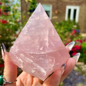 May include: A large, pale pink rose quartz pyramid crystal with a smooth, polished surface. The crystal is translucent and has a slight shimmer.