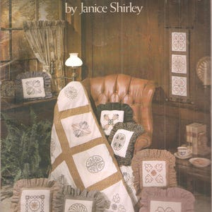 Puede incluir: Imagen de una portada de libro titulada "Traditional Candlewicking by Janice Shirley". La imagen muestra un edredón y varias almohadas decorativas con diseños bordados. Las almohadas tienen bordes con volantes y son en tonos marrones y blancos.