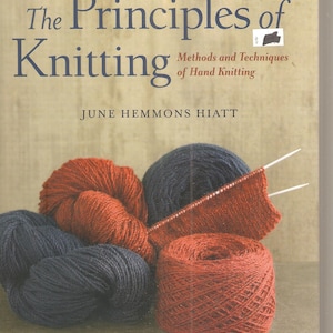 May include: A book titled "The Principles of Knitting" with the subtitle "Methods and Techniques of Hand Knitting" by June Hemmons Hiatt. The cover features skeins of red and navy blue yarn, with knitting needles and a swatch of knitted fabric.