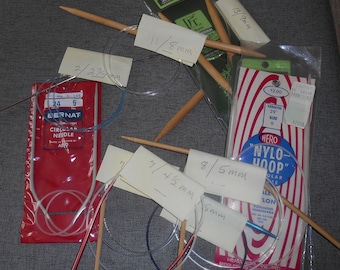May include: A collection of knitting needles and accessories, including wooden straight needles, circular needles, and a package of Hero Nyl-Hoop needles. Various sizes are indicated on attached labels, with measurements in inches and millimeters.