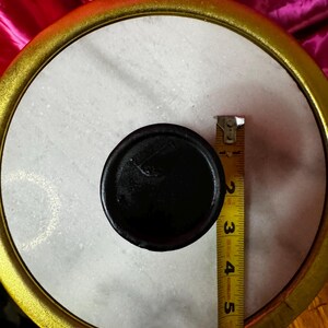 K&ouml;nnte beinhalten: Ein rundes Objekt aus wei&szlig;em Marmor mit einem schwarzen Mittelteil und einem goldfarbenen Rand. Ein Ma&szlig;band zeigt einen Durchmesser von etwa 12,7 cm. Es k&ouml;nnte sich um ein dekoratives Element oder einen Deckel handeln.