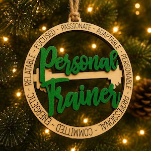May include: A circular wooden ornament featuring the green text Personal Trainer layered over a barbell graphic. The outer ring is engraved with the words Passionate, Adaptable, Personable, Professional, Committed, Energetic, Relatable, and Focused.