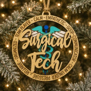 May include: A circular wooden ornament featuring the text Surgical Tech in script, a central caduceus symbol in teal and blue, and a border inscribed with the words Team Player, Calm, Empathetic, Goop, Communicator, Calm Under Pressure, Reliable, Organized.