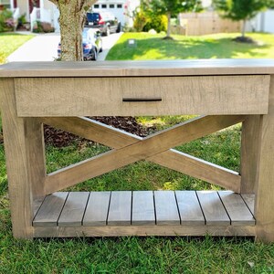 May include: A rustic wooden console table with a single drawer and a lower shelf. The table has a distressed gray finish and a criss-cross design on the legs.