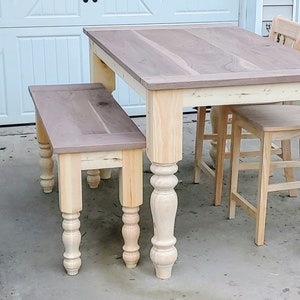May include: A wooden dining table set with a light brown top and turned legs. The table is accompanied by a matching bench and two chairs.